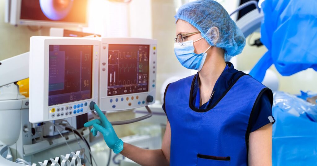 A woman in a blue uniform operates a computer, focusing on a medical ventilator in a MedTech environment.