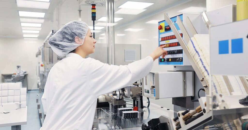 Woman in a lab coat engages with a machine, highlighting the critical role of MES in ensuring Quality Management.