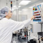 Woman in a lab coat engages with a machine, highlighting the critical role of MES in ensuring Quality Management.