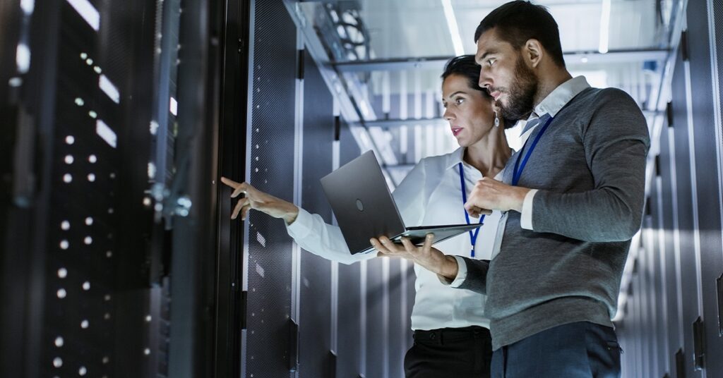 Two professionals analyzing data on a computer in a server room, focusing on advanced production planning and scheduling (APS)