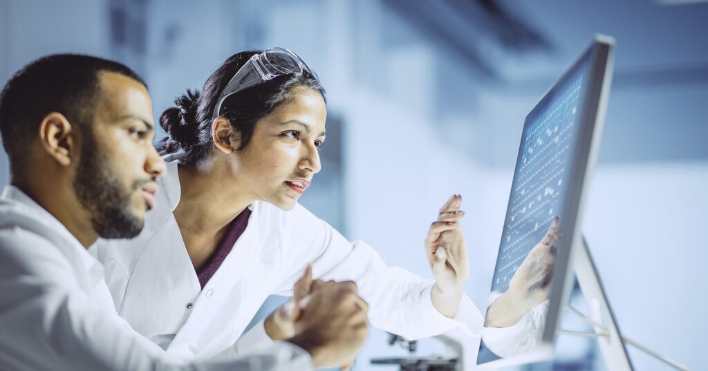 Two professionals in lab coats analyzing data on a computer screen, emphasizing a focus on MES and QMS processes.