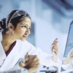 Two professionals in lab coats analyzing data on a computer screen, emphasizing a focus on MES and QMS processes.