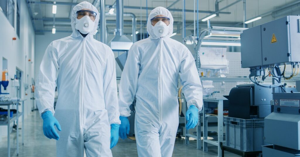 Two engineers / scientists wearing Hazmat Suits, while walking through technologically advanced laboratory. The environment emphasizes safety and resilience in operations.