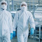 Two engineers / scientists wearing Hazmat Suits, while walking through technologically advanced laboratory. The environment emphasizes safety and resilience in operations.