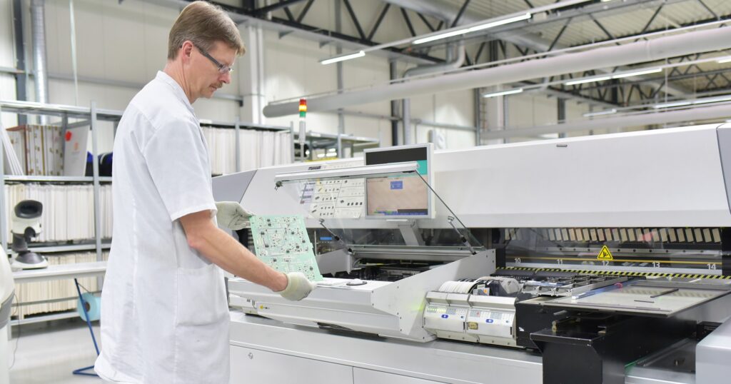 A man in a white lab coat operates a machine, focusing on electronics for new product introduction (NPI).