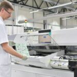 A man in a white lab coat operates a machine, focusing on electronics for new product introduction (NPI).