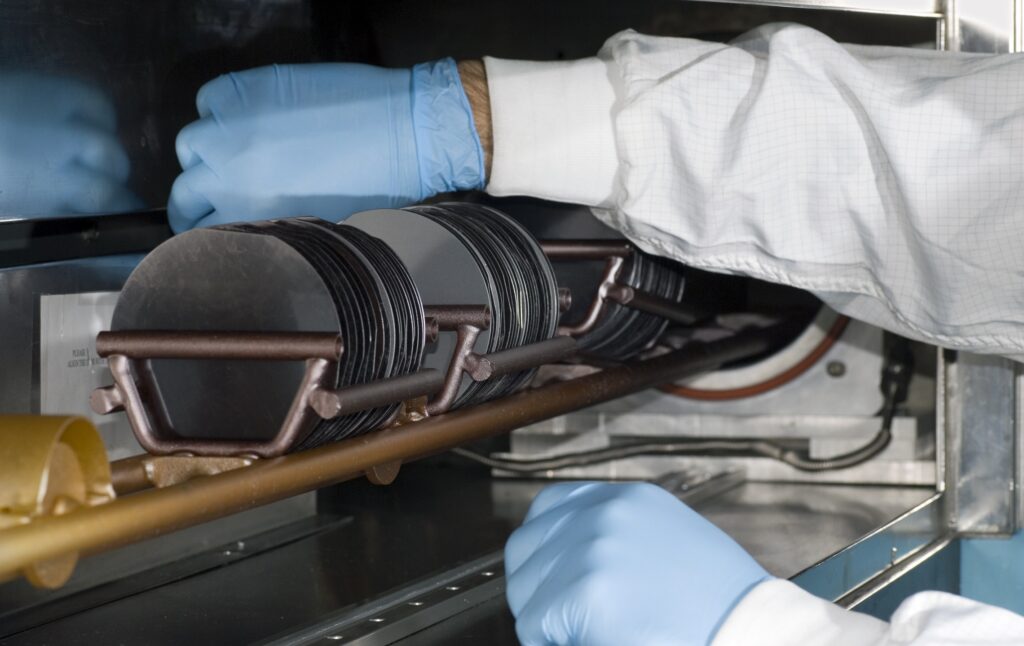 A person dressed in a white coat carries silicon wafers, carefully handling it in a semiconductor work