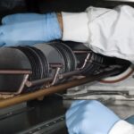 A person dressed in a white coat carries silicon wafers, carefully handling it in a semiconductor work