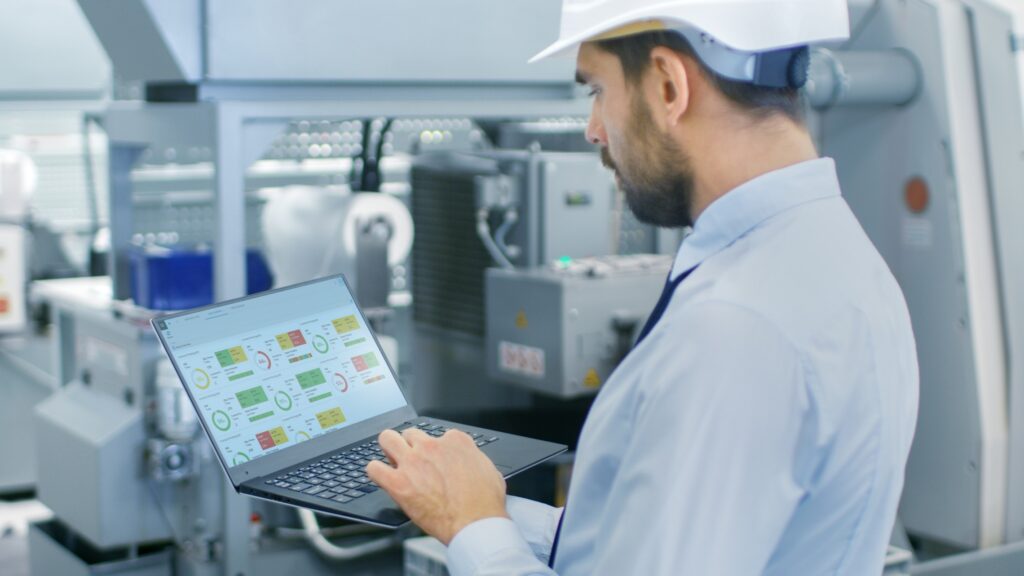 A man in safety gear, including a hard hat , is engaged with a laptop, showcasing MES Platform.