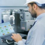 A man in safety gear, including a hard hat , is engaged with a laptop, showcasing MES Platform.