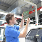 Male worker analyzing a semiconductor piece, in a factory.