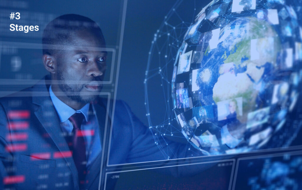 A man in a suit sitting in front of a large screen with a globe on it, with a serious expression on his face. The globe is surrounded by multiple screens, each displaying a different image of the world, and, on the top left corner, it has “Stages”, which may highlight the stages of the multisite MES project.