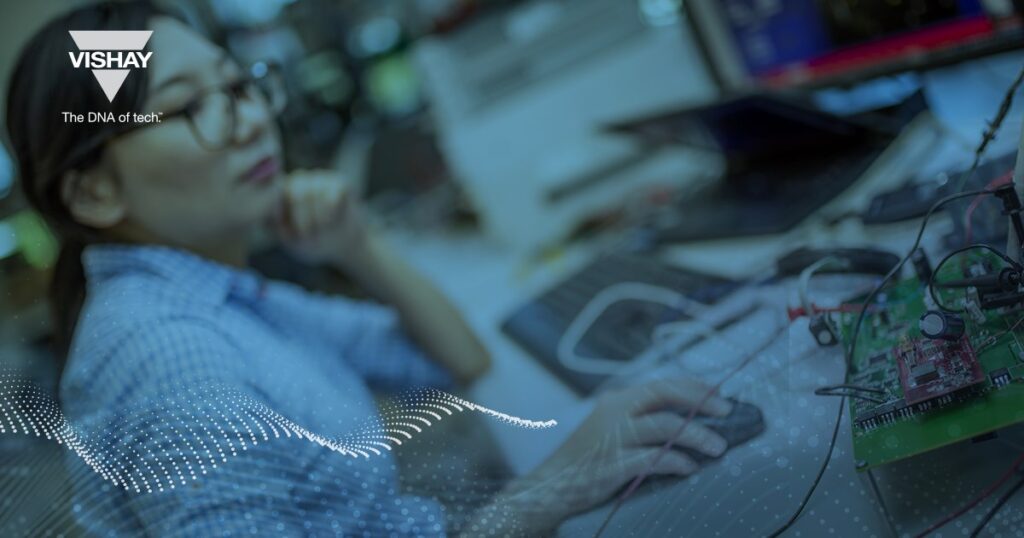 Woman wearing glasses interacting with her laptop mouse, pursuing manufacturing excellence, with Vishay logo visible in the left top corner.