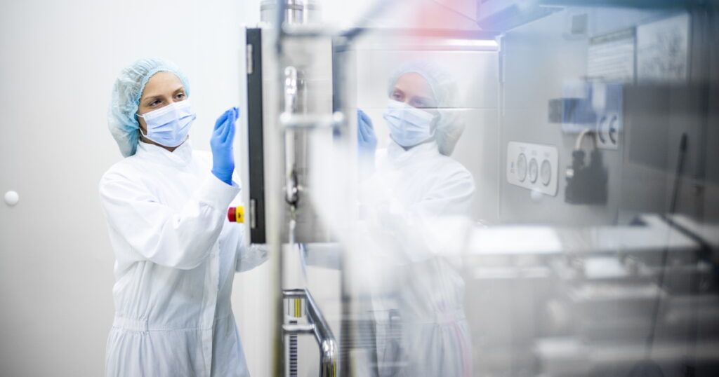 A woman in a lab coat and gloves inspects a machine, highlighting the importance of quality in the MedTech industry.