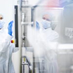 A woman in a lab coat and gloves inspects a machine, highlighting the importance of quality in the MedTech industry.